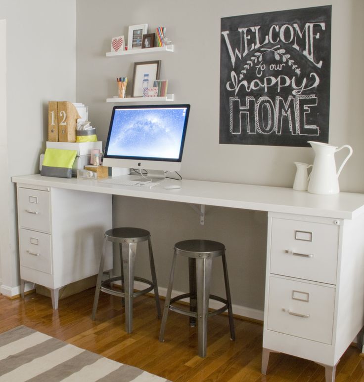 a white desk with two stools and a computer on it in front of a chalkboard