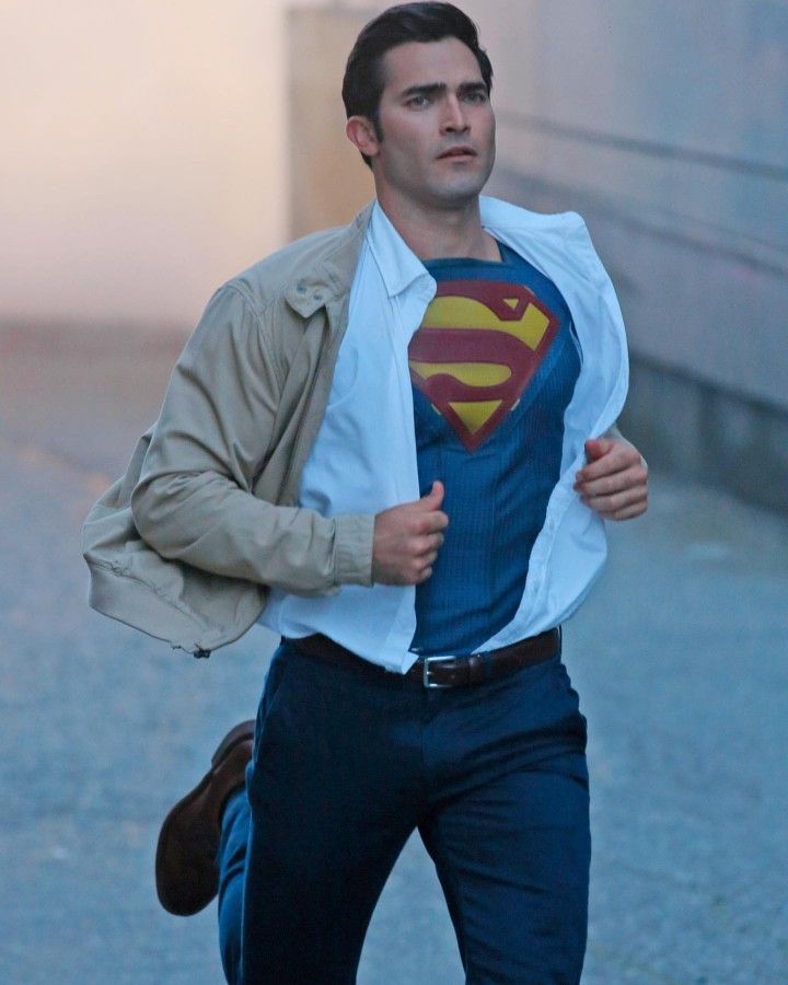 a man in a superman t - shirt is running on the street with his jacket over his shoulders