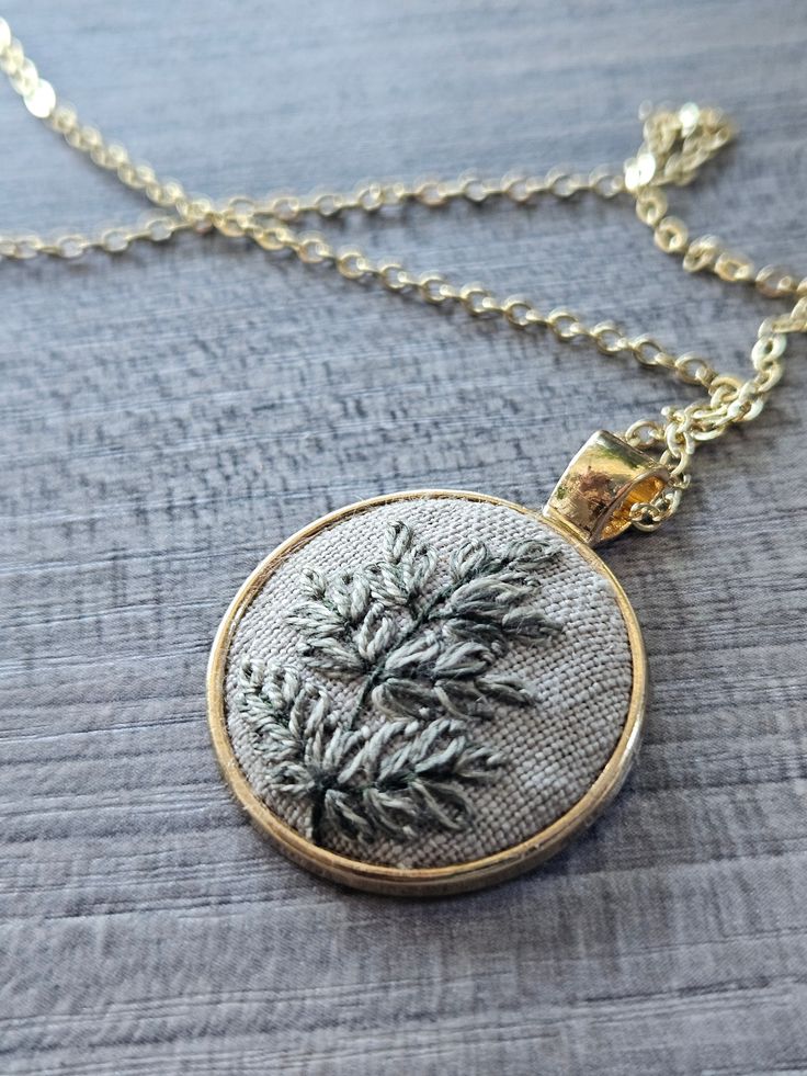 The pendant was hand embroidered by myself and would make the perfect gift for the nature lover or outdoor enthusiast in your life. Main Features: - Pendant was designed and hand embroidered by myself - The fern was embroidered using DMC thread on grey linen - Pendant measures 1" in diameter - The pendant and chain are gold If you are giving this as a gift and would like a note attached, please let me know. Instagram: Follow me @lemonsandthreadco for more embroidery content Contact: If you have Fern Jewelry, Nature-inspired Pendant Necklace With Hand Painted Details, Embroidered Necklace Pendant, Nature-inspired Hand Painted Pendant Necklace, Linen Pendant, Nature-inspired Pendant Jewelry With Pressed Flowers, Dmc Thread, Gray Linen, Gold Pendant