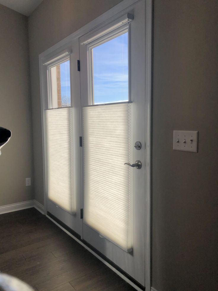 an empty room with two doors and blinds on the windows, in front of a white door