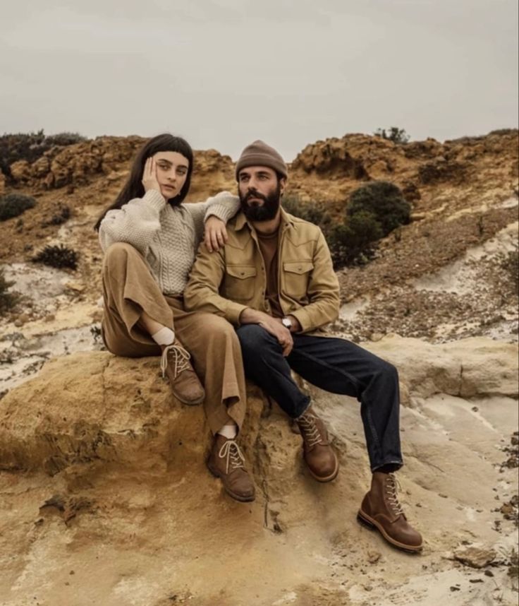 a man and woman sitting on top of a large rock in the middle of nowhere