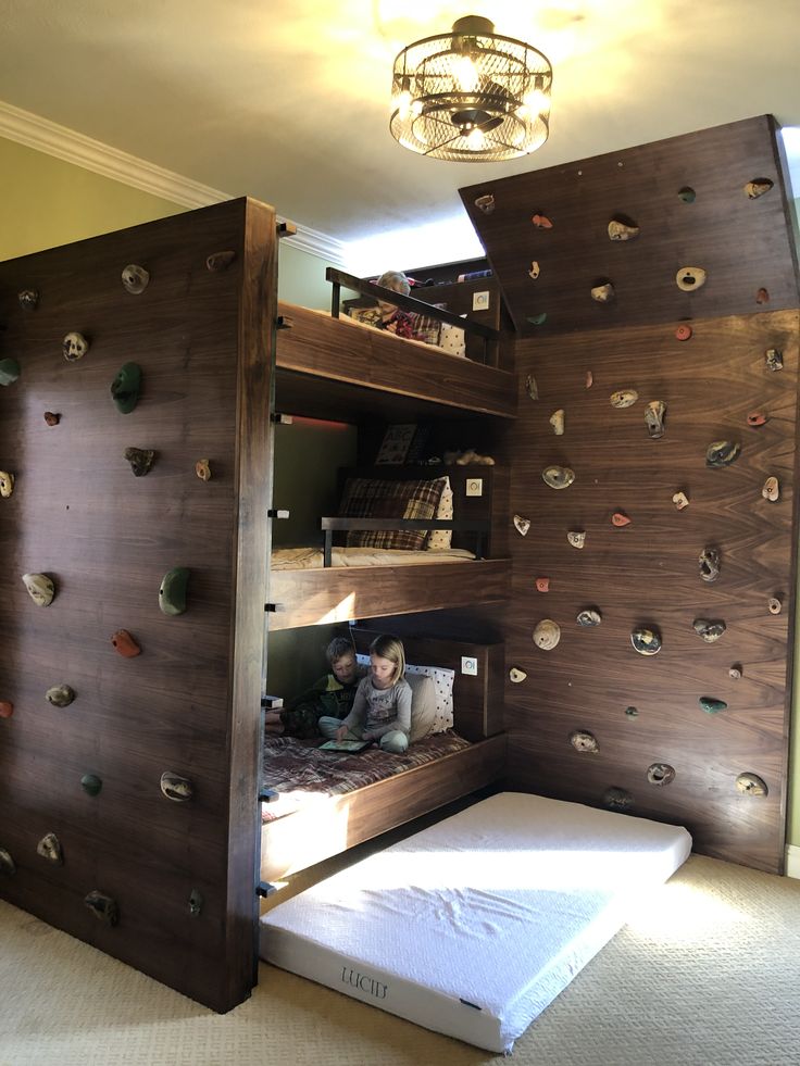 there is a child sitting on the bottom bunk bed in this room with climbing walls