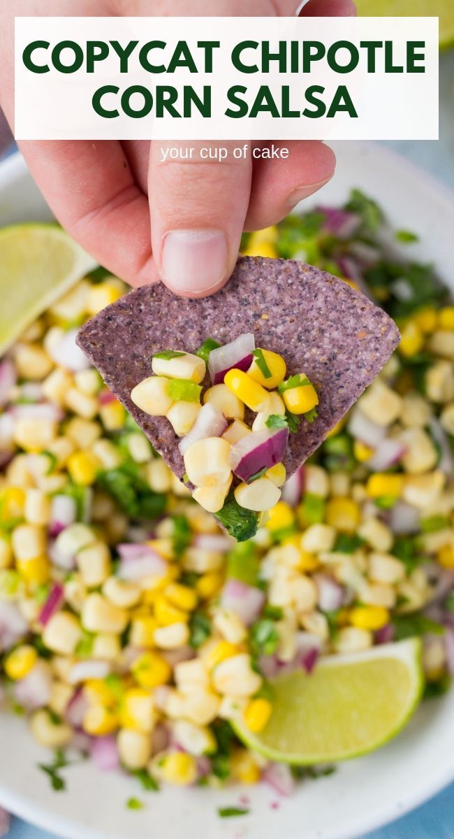 corn salsa in a white bowl with a tortilla chip being held over it