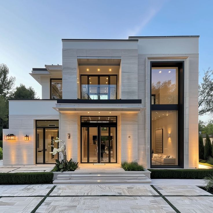 a large modern house with lots of windows and lights on the front door, surrounded by greenery