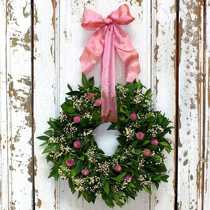 a wreath hanging on the side of a white door with a pink bow around it