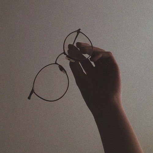 a hand holding up a pair of glasses against a gray sky with the light coming through it