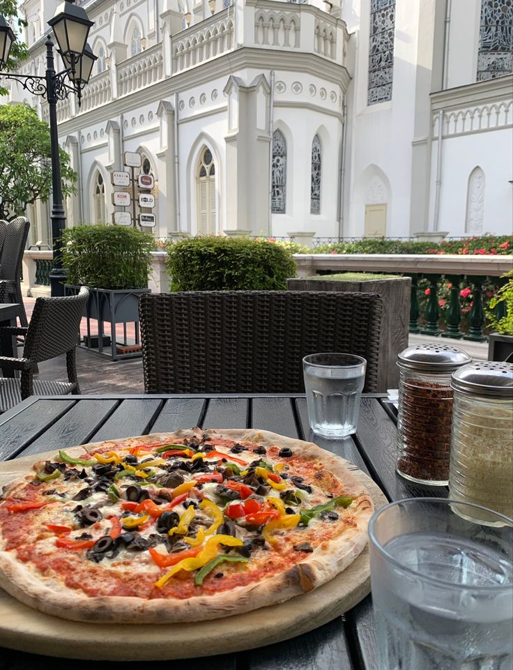 a pizza sitting on top of a wooden table next to water glasses and an umbrella