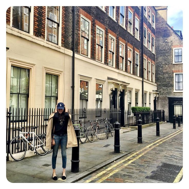 a woman is standing on the sidewalk next to her bike and some buildings in london