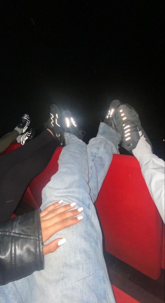 two people sitting on a red couch with their feet up and one person wearing black shoes