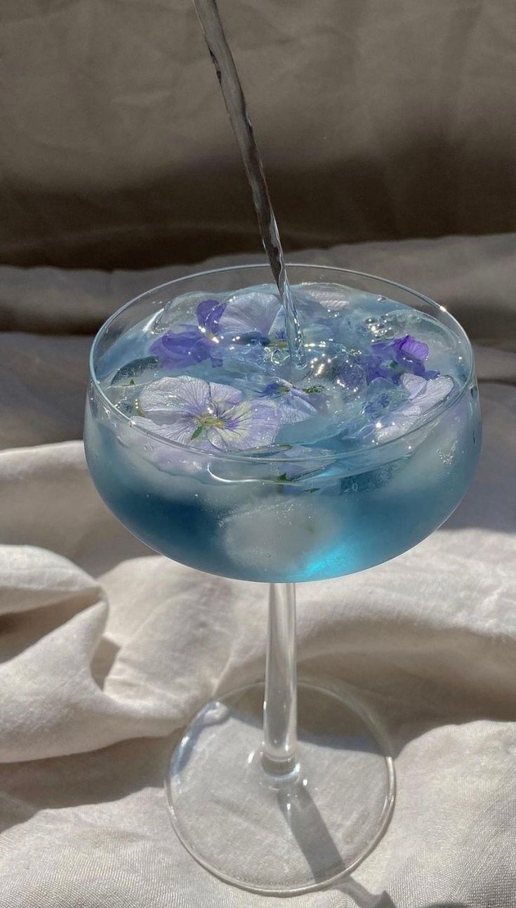 a glass filled with blue liquid sitting on top of a white cloth covered tablecloth