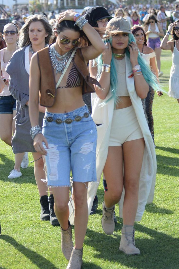 two women walking on the grass at a music festival with other people in the background