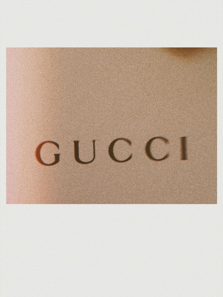 the word gucci written in cursive writing on a white surface with an orange light behind it