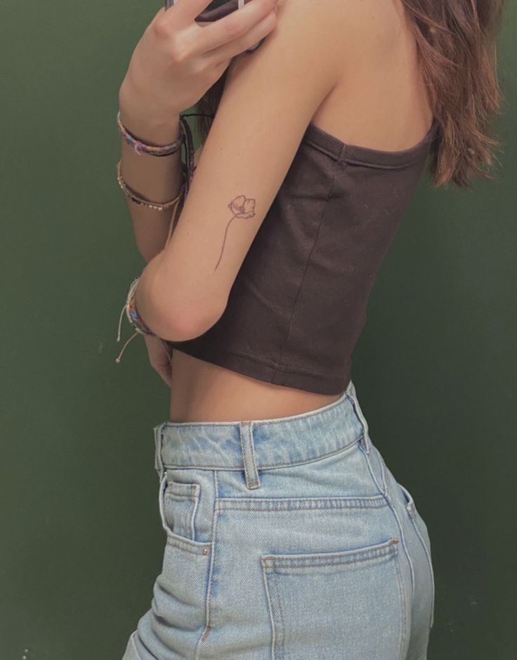 a woman with a tattoo on her arm looking at her cell phone while leaning against a wall