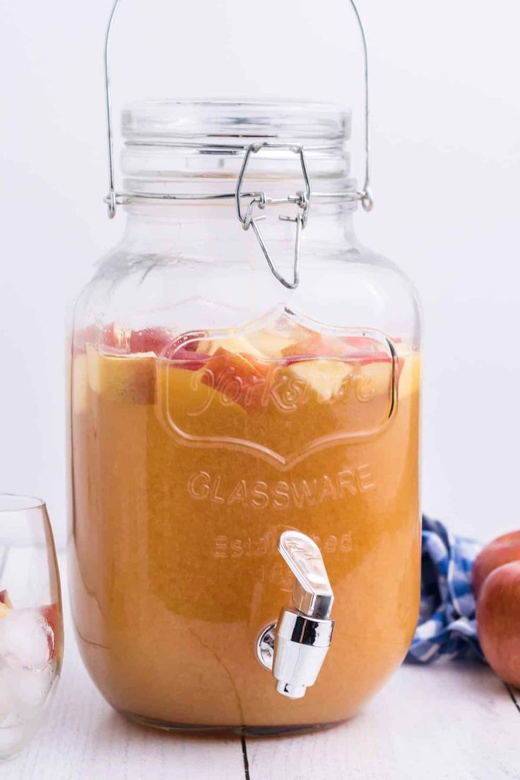 a glass jar filled with liquid next to apples