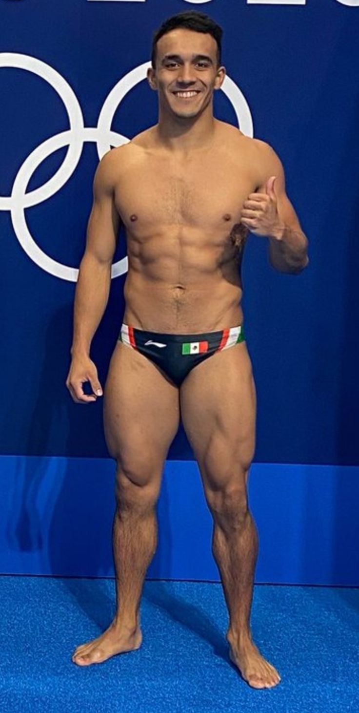 a man with no shirt standing in front of a blue wall and posing for the camera