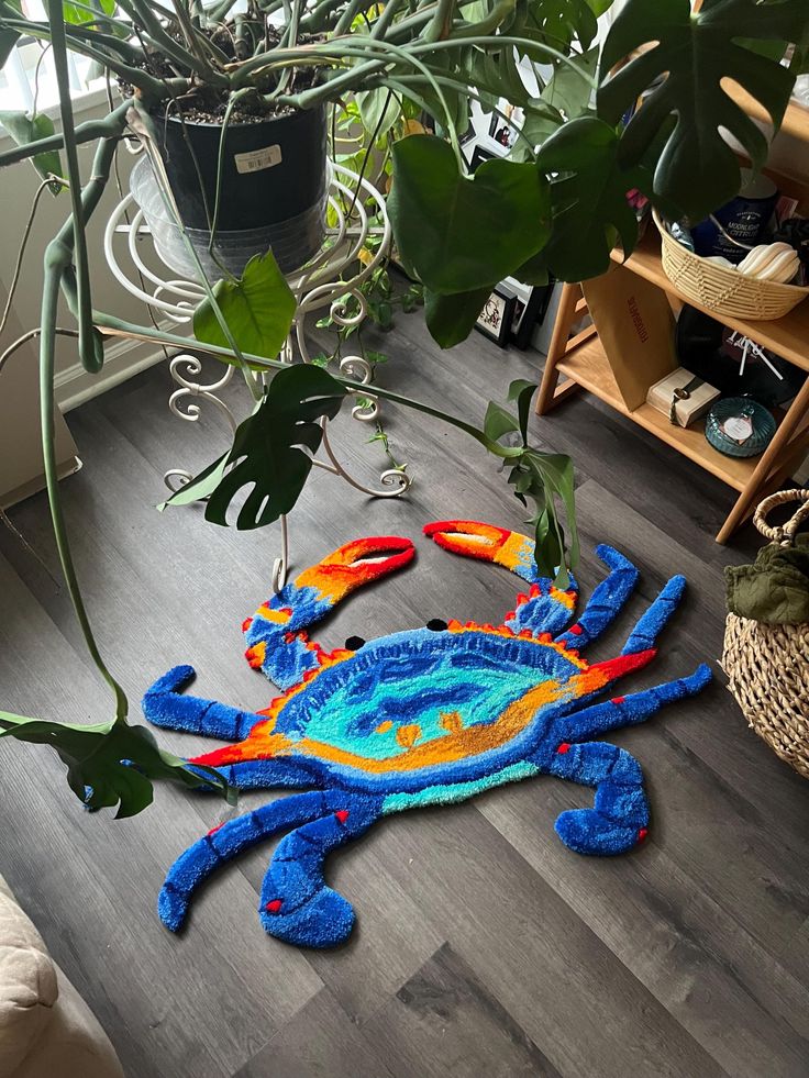 a blue and orange crab rug on the floor next to a potted plant