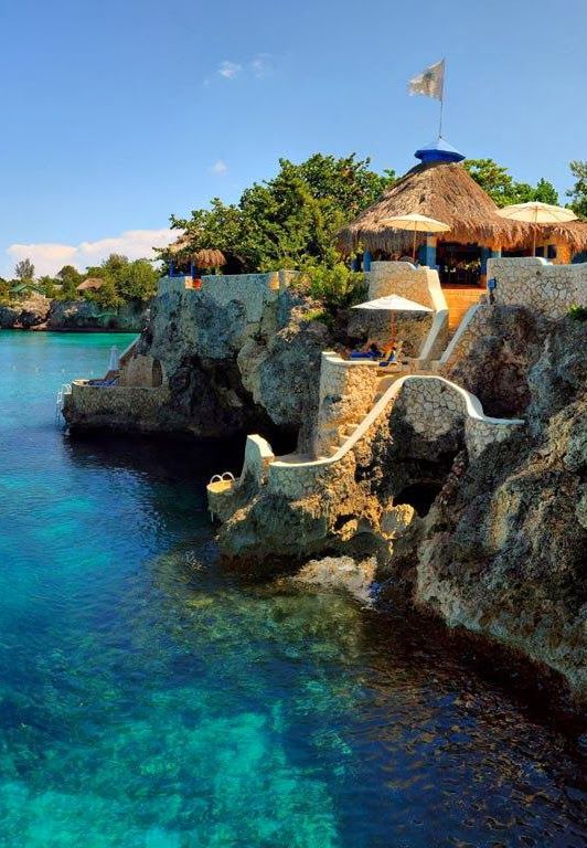 the water is crystal blue and there are umbrellas in the shade on the rocks