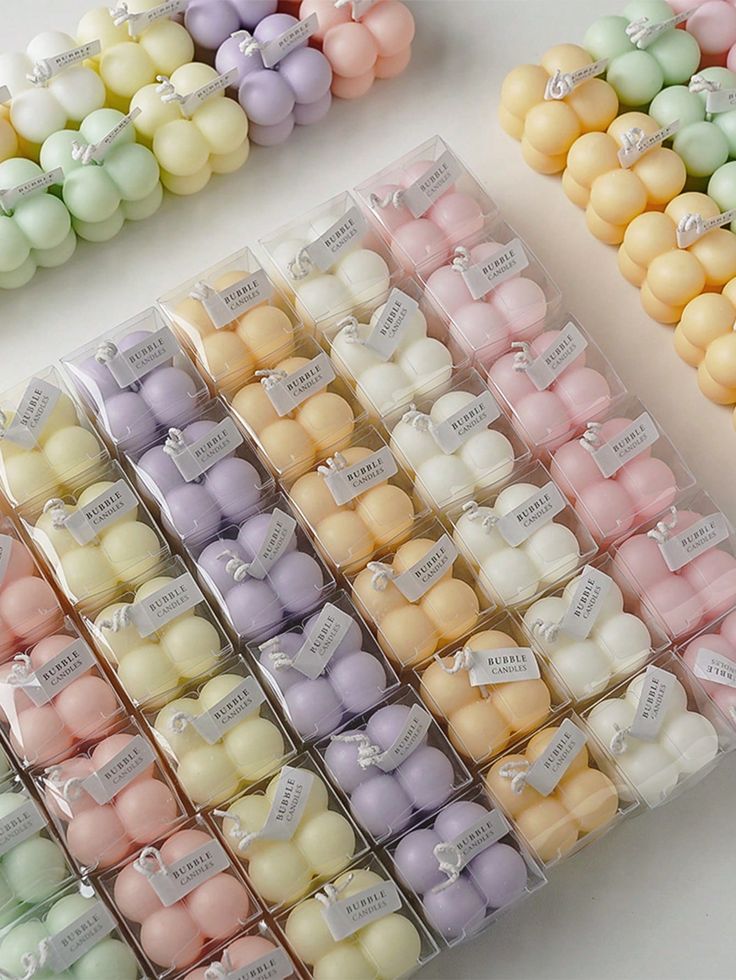 several rows of small pastel colored candles in plastic containers on a white table top