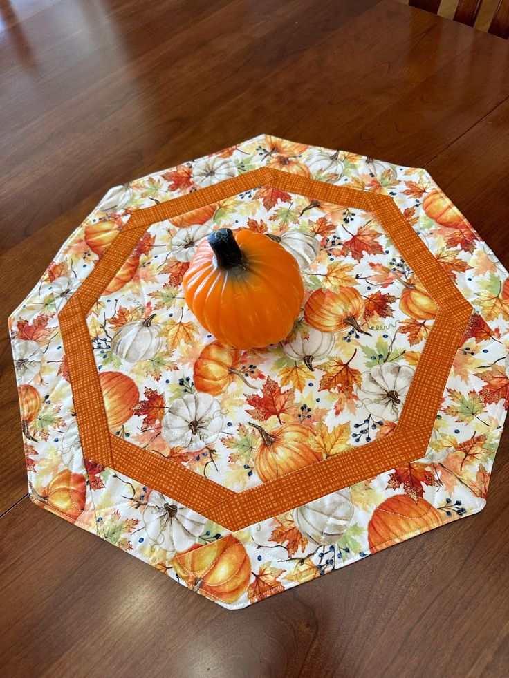 an orange pumpkin sitting on top of a quilted tablecloth covered in fall leaves