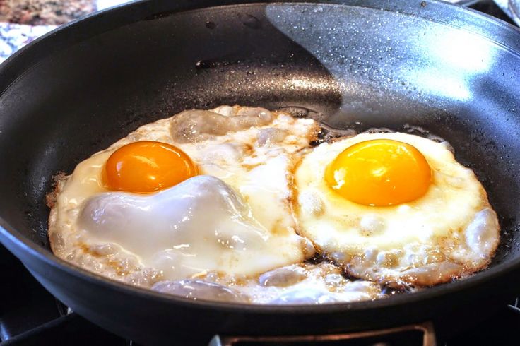 two fried eggs cooking in a skillet on the stove