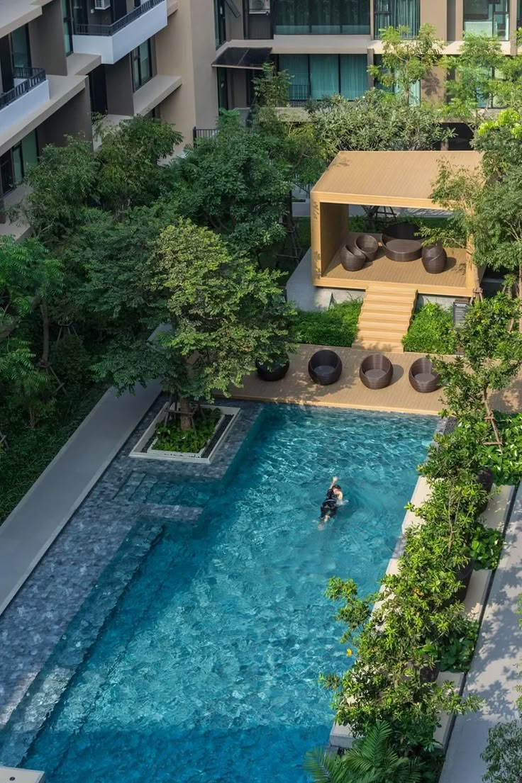 an aerial view of a pool surrounded by trees and buildings with a person swimming in it