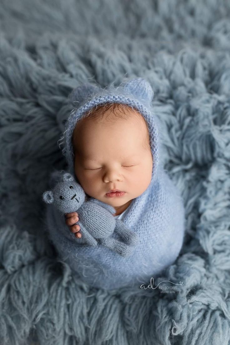 a baby wrapped in a blue blanket holding a teddy bear