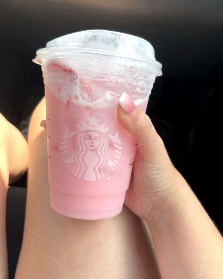 a woman's hand holding up a pink starbucks drink