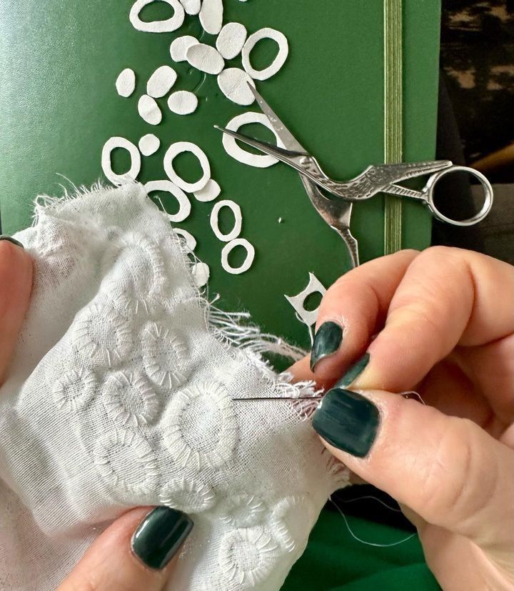 someone is using scissors to cut fabric on a piece of cloth with white flowers in the background