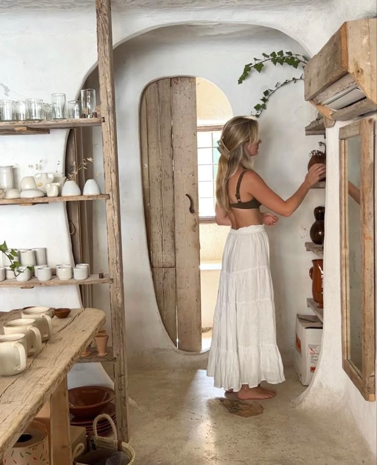 a woman in a white dress is looking at the shelves and doors that are open