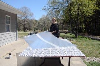 a woman standing next to a table with a sheet on top of it in front of a house