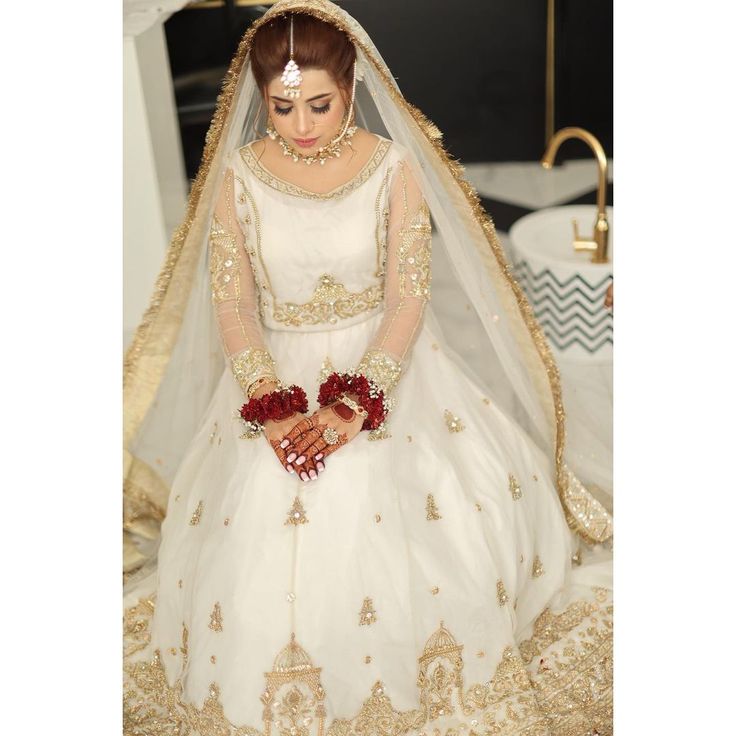 a woman in a white and gold bridal gown with red flowers on her hands