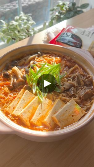 a bowl of soup with tofu and vegetables in it on a table next to a book