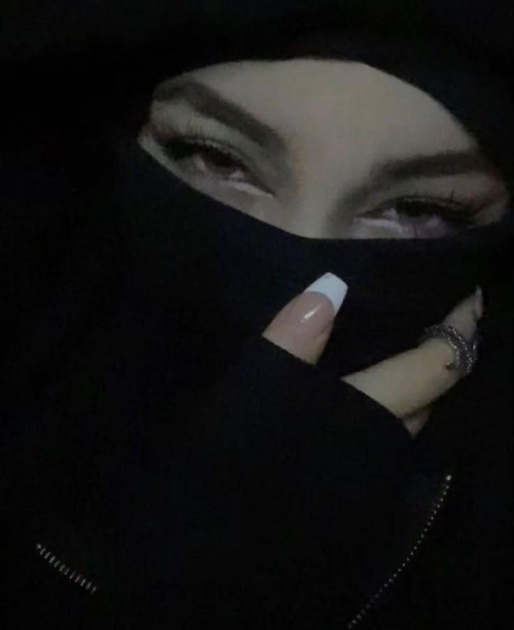 a woman wearing a black hijab and holding her finger up to her face