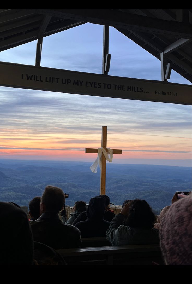 people are sitting at the top of a hill with a cross in front of them