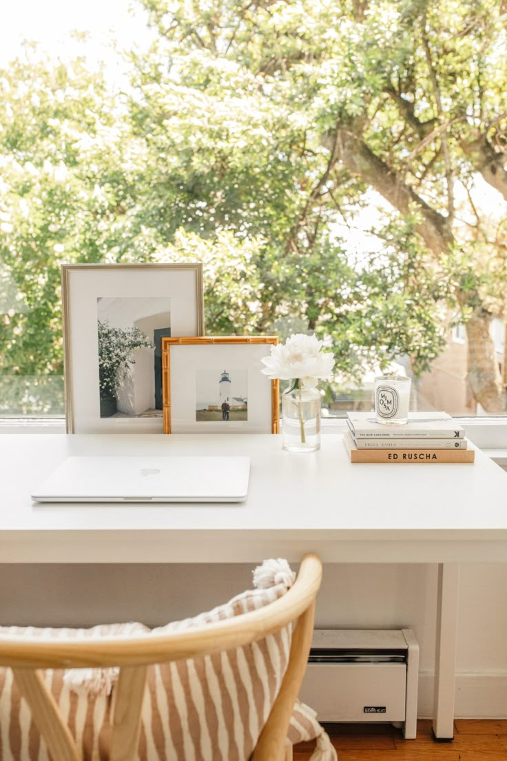 a white desk topped with a laptop computer sitting next to a window covered in trees