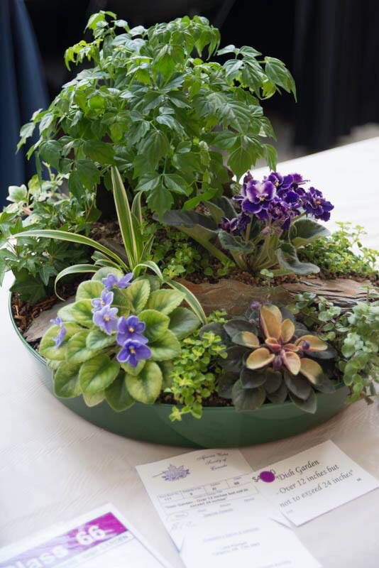 an arrangement of flowers and plants in a green bowl on a table with some cards