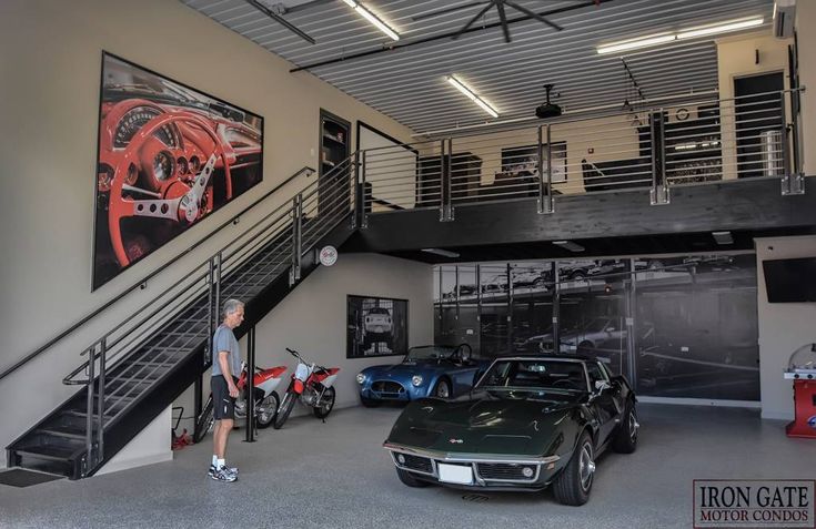 a man standing next to two cars in a garage with stairs leading up to the second floor