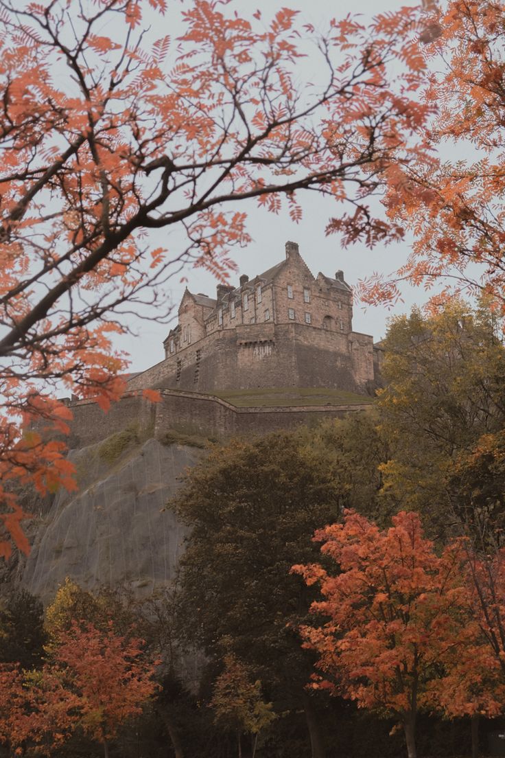 an old castle on top of a hill surrounded by trees with orange leaves in the foreground