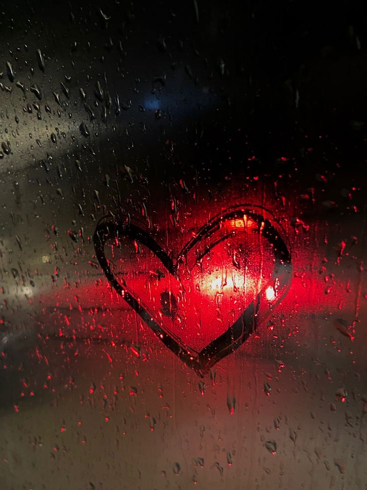 a red heart shaped light sitting on top of a rain covered window