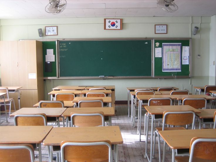 an empty classroom with wooden desks and green chalkboard