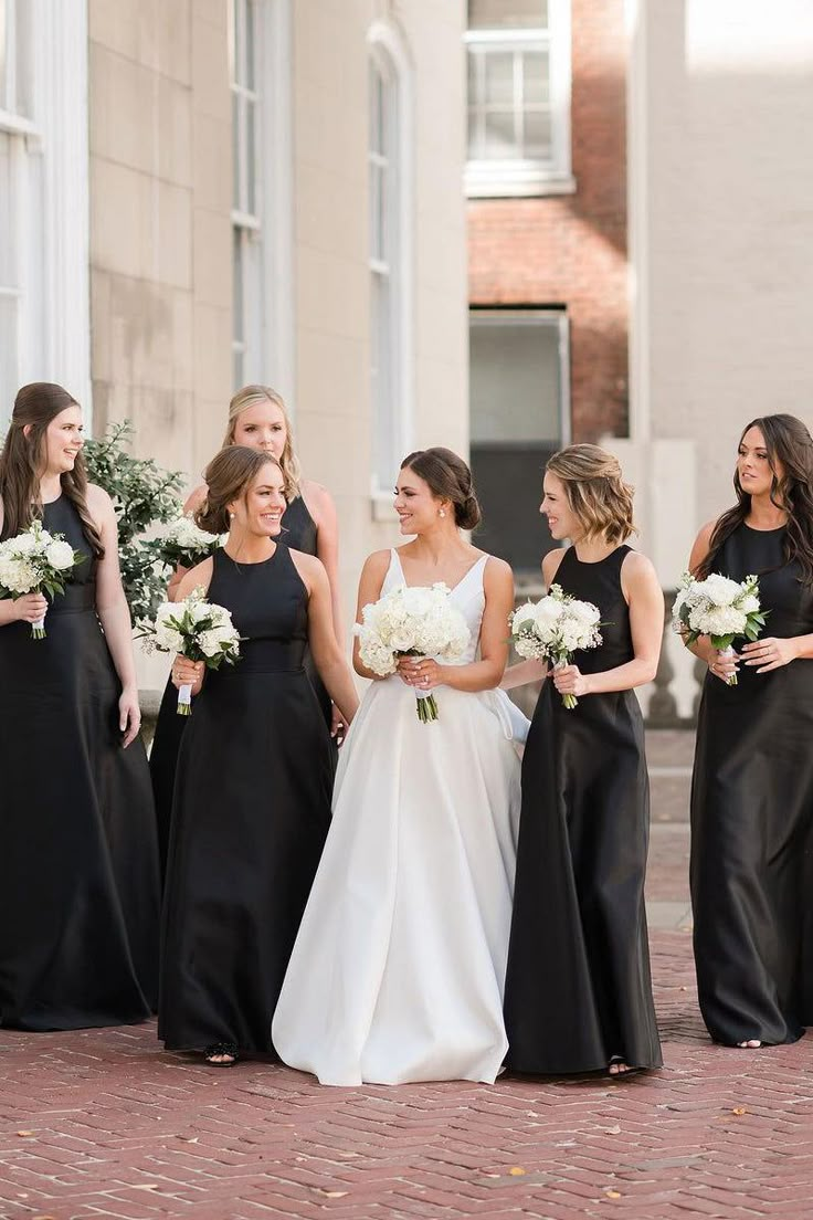 a group of women standing next to each other wearing black dresses and holding bouquets