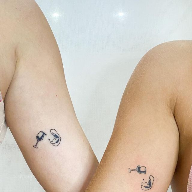 two women with tattoos on their arms holding wine glasses