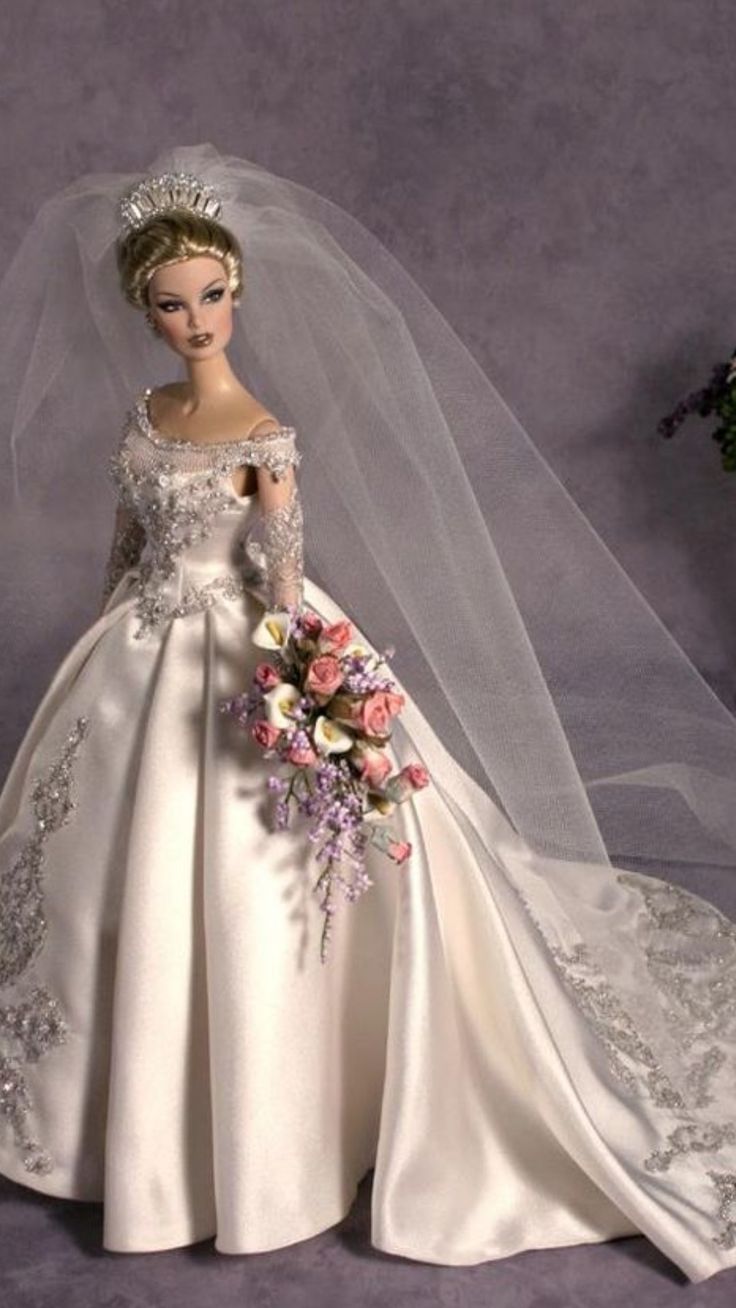 a barbie doll dressed in a wedding gown and veil with flowers on the side, holding a bridal bouquet