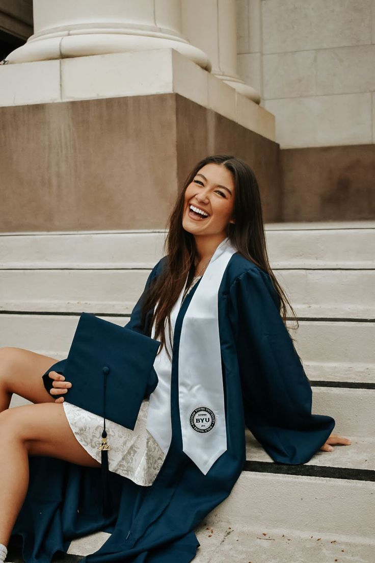 a woman sitting on the steps with her graduation cap and gown over her shoulder, smiling