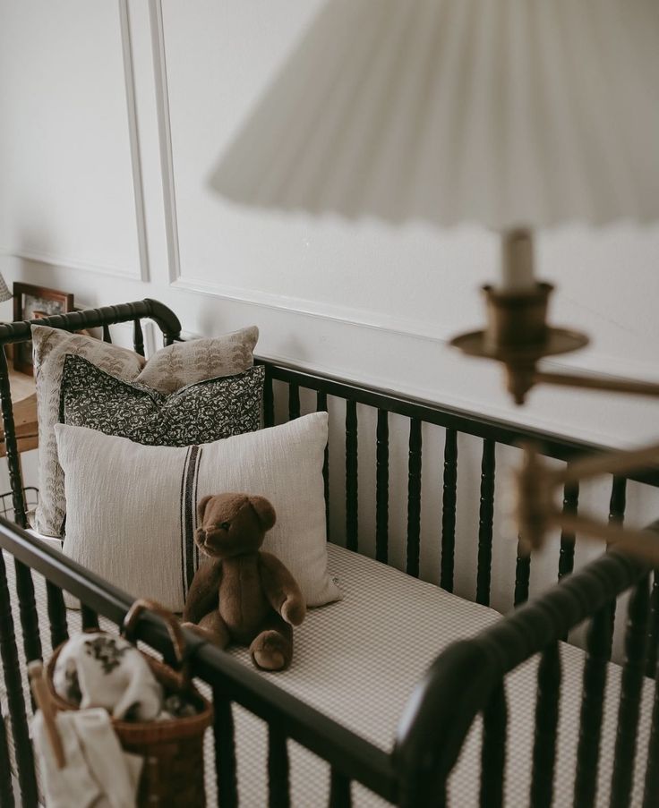 a teddy bear sitting on top of a crib next to pillows and a lamp