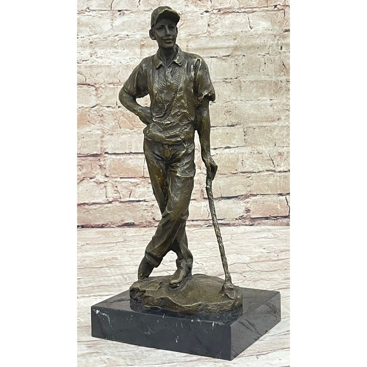 a bronze statue of a man holding a golf club and wearing a hat, standing in front of a brick wall