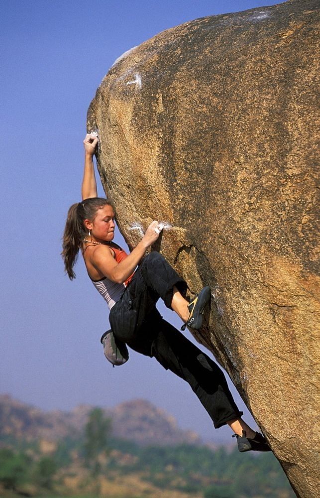 a woman climbing up the side of a large rock