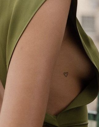 a woman with a small heart tattoo on her left side chest, wearing a green dress