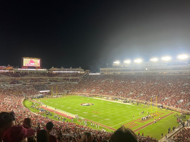 a large stadium filled with people watching a football game on the field at night time