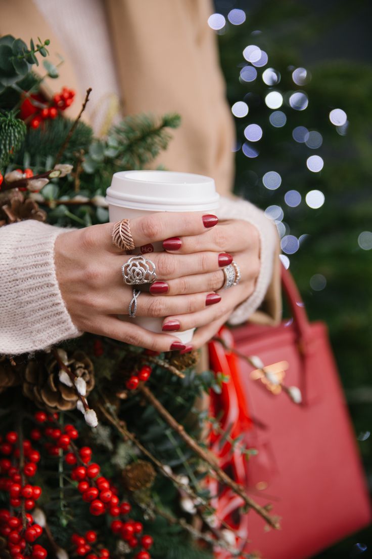 a woman holding a cup of coffee in her hands with christmas decorations on the background